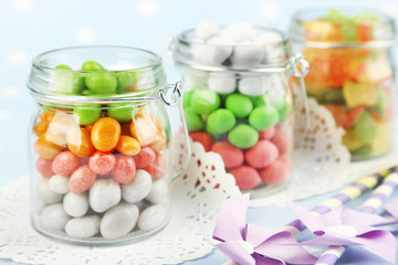 Multicolor candies in glass jars on colorful background