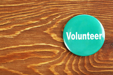 Round volunteer button on wooden background