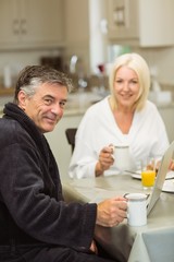 Mature couple having breakfast together man using laptop