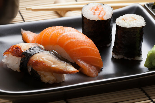 Japanese sushi: nigiri and maki on black plate.