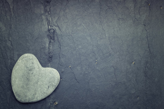 Gray zen heart shaped rock in the corner on a tile background
