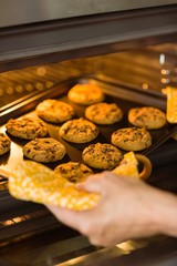 Woman taking tray of fresh cookies out of oven
