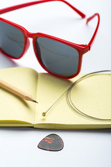 Yellow notepad with pencil, sunglasses, string and mediator