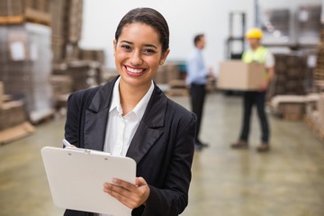 Smiling warehouse manager writing on clipboard