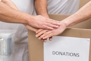 Volunteer team holding hands on a box of donations