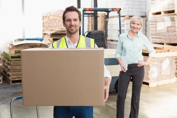 Smiling warehouse worker carrying box