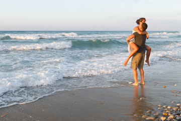 Fototapeta na wymiar Young couple enjoys walking on a hazy beach at dusk.