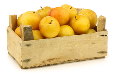 fresh yellow plums in a wooden crate on a white background
