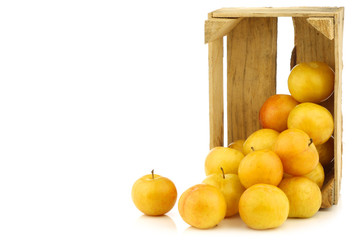 fresh yellow plums in a wooden crate on a white background