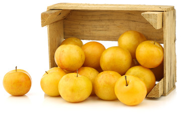 fresh yellow plums in a wooden crate on a white background
