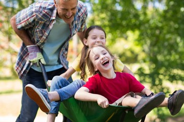 Happy father and his children playing with a wheelbarrow