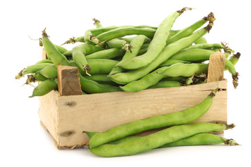 bunch of broad beans in a wooden box on a white background