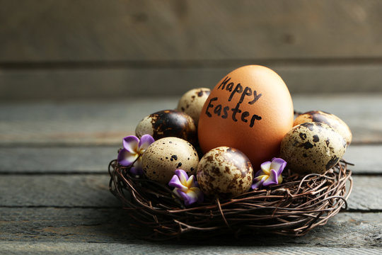 Bird eggs with decorative flowers in nest on wooden background