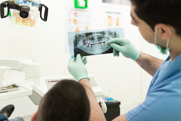 Dentist Holding X-Ray And Examse White Patient