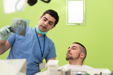 Dentist Holding X-Ray And Examse White Patient