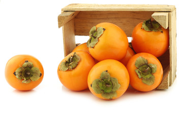 fresh kaki fruit in a wooden crate on a white background