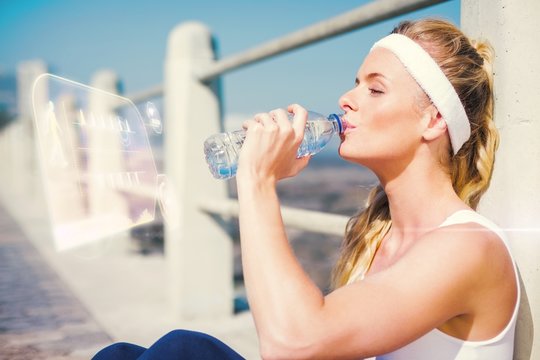 Composite image of fit blonde sitting on the pier drinking water