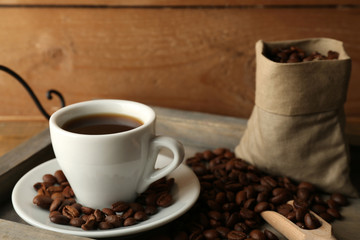 Cup of coffee with beans on tray and rustic wooden background