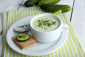 Cucumber soup in bowl on color wooden table background