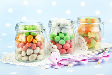 Multicolor candies in glass jars on colorful background