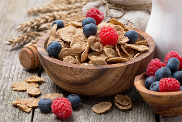 wholegrain flakes with berries and jug of milk on wooden table