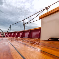 Papier Peint photo Naviguer Wood deck of a sailboat at sea under stormy skies. Square format