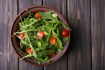 Salad with arugula and cherry tomatoes on wooden table