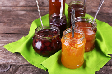 Jars of tasty jam with napkin on wooden background