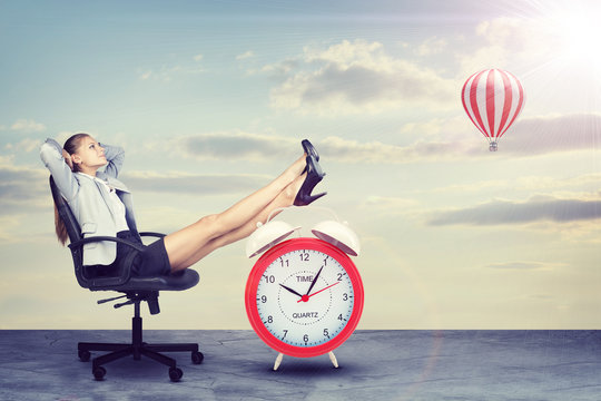 Businesswoman Sitting With Her Feet Up On Alarm-clock