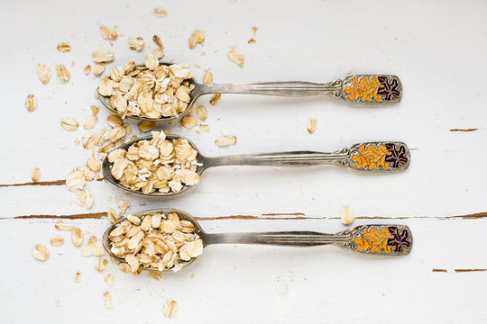 Three tablespoons of oatmeal lying on a white wooden background