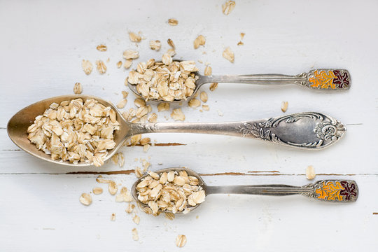 Three tablespoons of oatmeal lying on a white wooden background