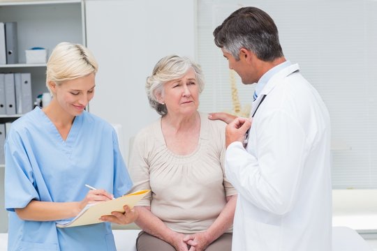 Doctor consoling patient while nurse writing reports