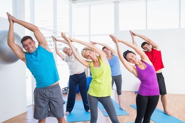 Fototapeta premium Happy people doing stretching exercise in yoga class