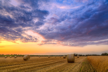 Sunset over farm field with hay bales