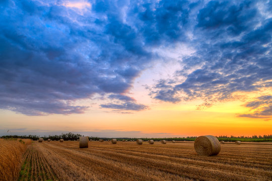 Sunset over farm field with hay bales