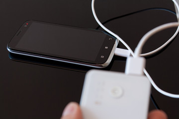 Male hand is holding power bank is charging smartphone