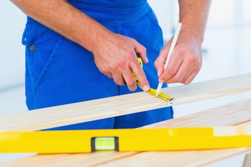 Carpenter marking on plank with tape measure