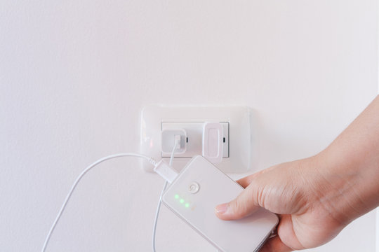 female hand plugging in the plug of her power bank in a socket