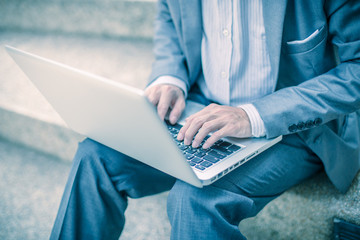 Businessman using laptop pc. He is sitting on a stairs.