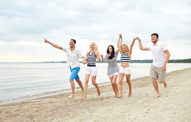 smiling friends in sunglasses running on beach