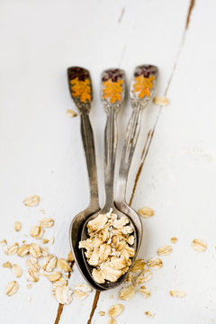 Three tablespoons of oatmeal lying on a white wooden background.