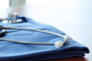 Stethoscope with blue doctor coat on wooden table with shallow D