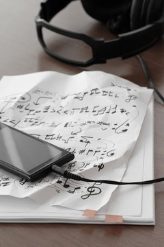 Closeup of smartphone with headphone on musical notes paper on w