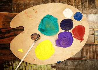 Wooden art palette with paint and brush on vintage background