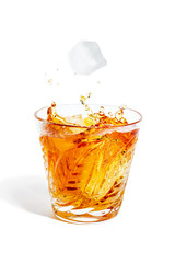 Ice cube falls with splashes into the glass with alcohol