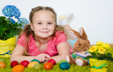Fototapeta na wymiar Smiling little girl lying with Easter eggs and flowers on green