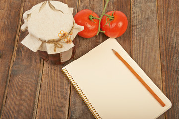 Conservation, tomato and notebook with pencil wooden background