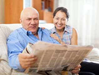 Portrait of laughing mature woman and elderly man with newspaper