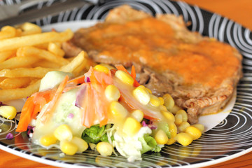 Steaks, french fries with vegetables salad on a plate.
