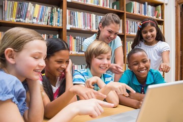 Cute pupils using tablet computer in library